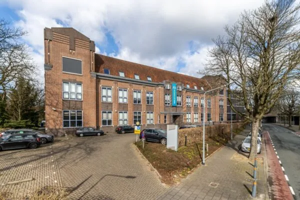 Vooraanzicht van een karakteristiek bakstenen kantoorgebouw aan de Lage Naarderweg met parkeerplaatsen en fietsenstalling.